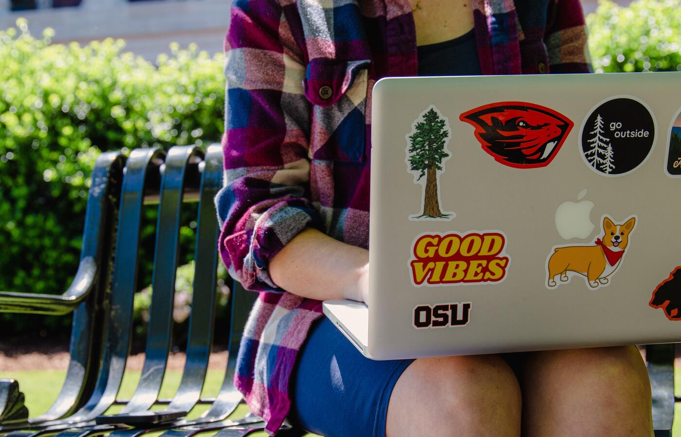 Students sits on outside bench with laptop on lap.