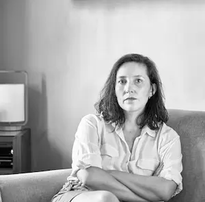 Black and white photo of Paz Peña sitting on a sofa with her arms crossed.